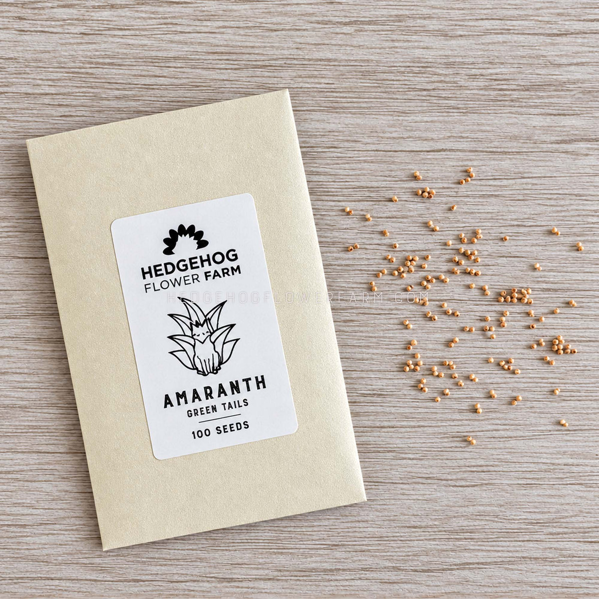 Photo of seed packet with label Hedgehog Flower Farm Amaranth Green Tails 100 seeds on the left and small, loose seeds of amaranth to the right against a wood textured background