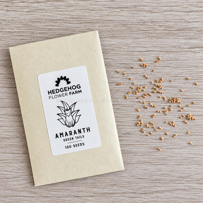 Photo of seed packet with label Hedgehog Flower Farm Amaranth Green Tails 100 seeds on the left and small, loose seeds of amaranth to the right against a wood textured background